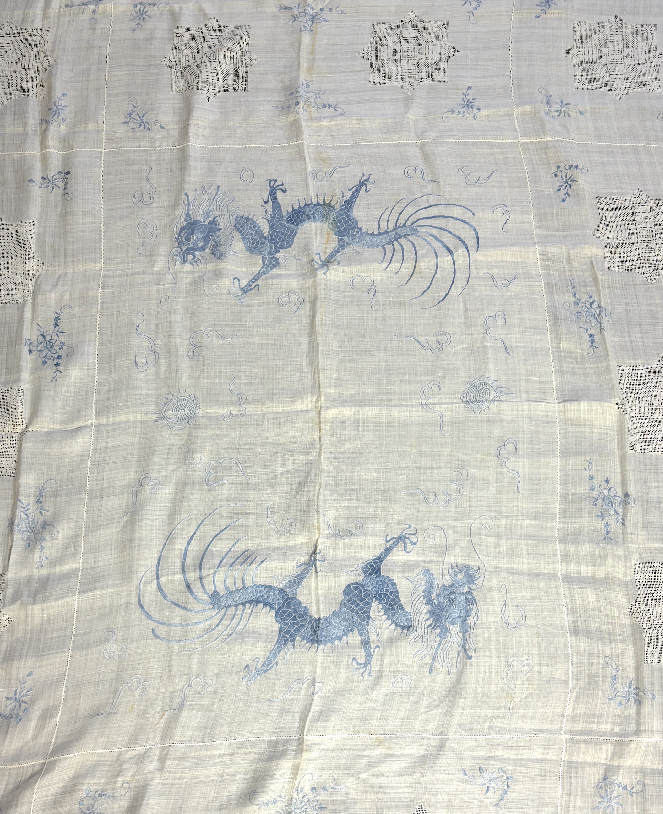 Chinese dragon and floral embroidered linen comprising two Chinese hand embroidered table cloths, both embroidered with blue dragons and flowers, together with a similar embroidered pillow case, a smaller cloth with whit
